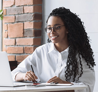 African-American female seated on laptop holding pen and smiling