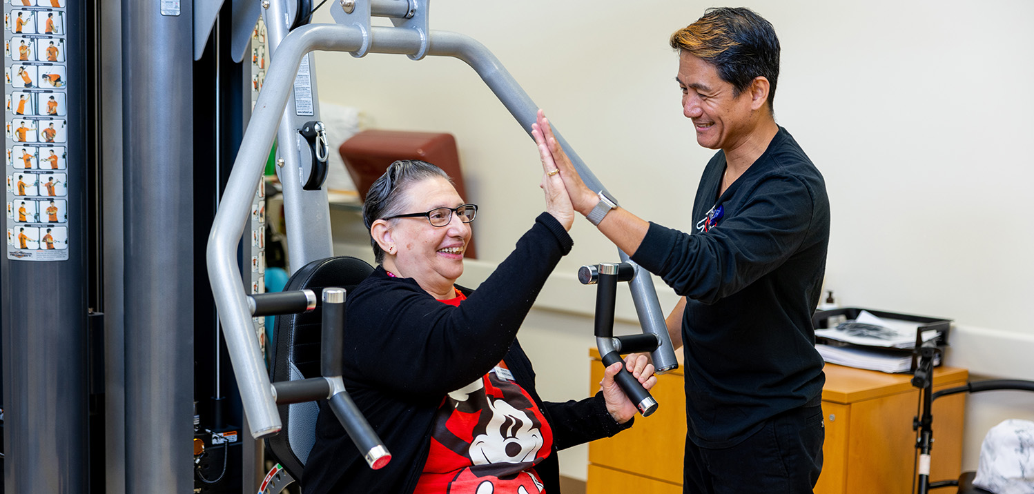 PT assisting participant using weight machine in PT area high fiving