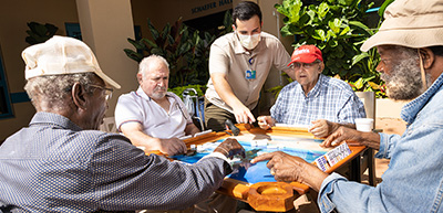 Group of participants playing dominoes outside with aide