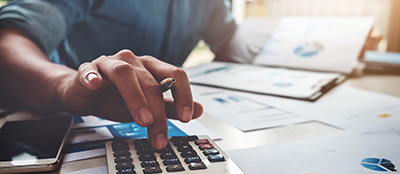 man typing on calculator with charts and graphs nearby