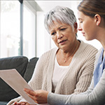 Senior female sitting on couch with caregiver, discussing paperwork