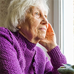 white female in purple sweater staring out window at home